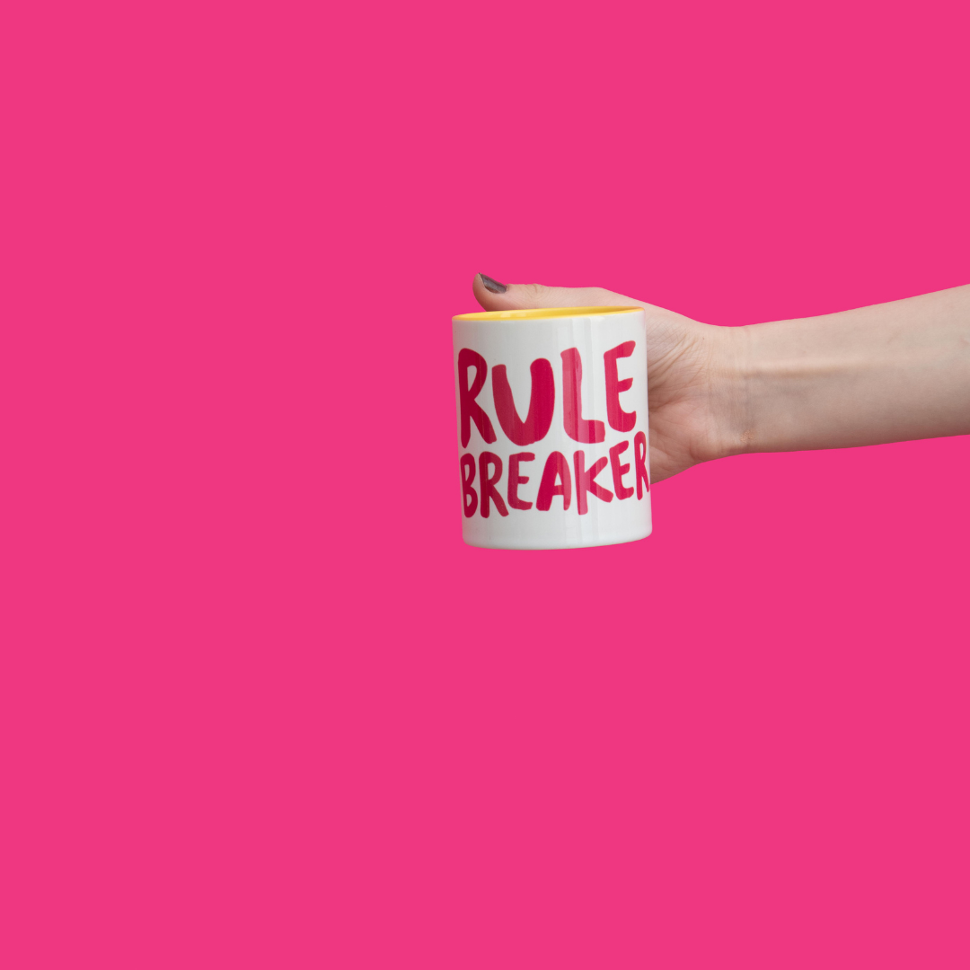A person holding Mug with Rule Breaker logo and yellow inside