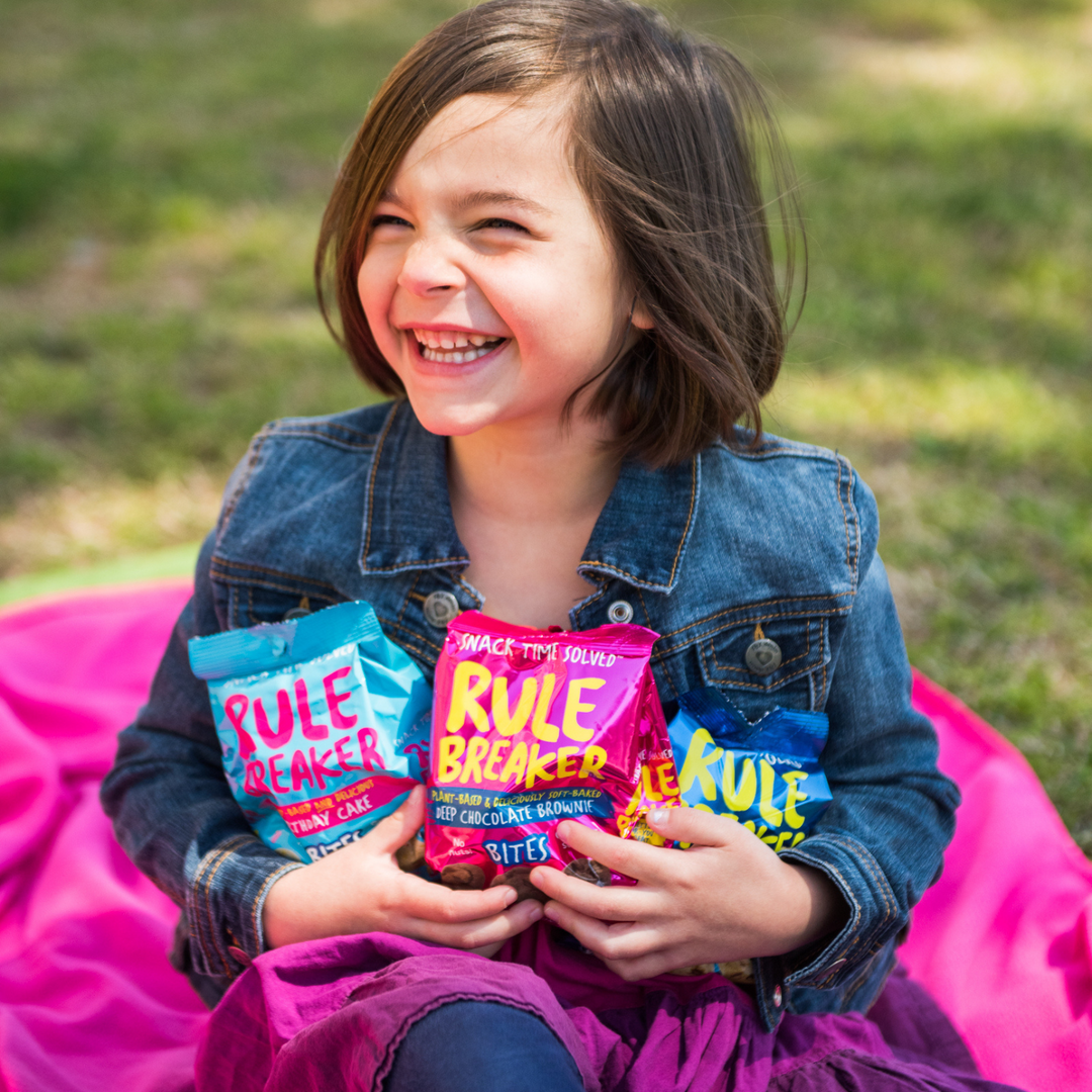 Girl holding Rule Breaker Snacks Bites bags Brownie Blondie Birthday Cake vegan gluten free allergen free